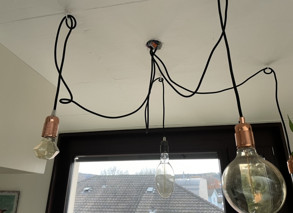 Drei Glühbirnen an schwarzen Kabeln als Pendelleuchte montiert